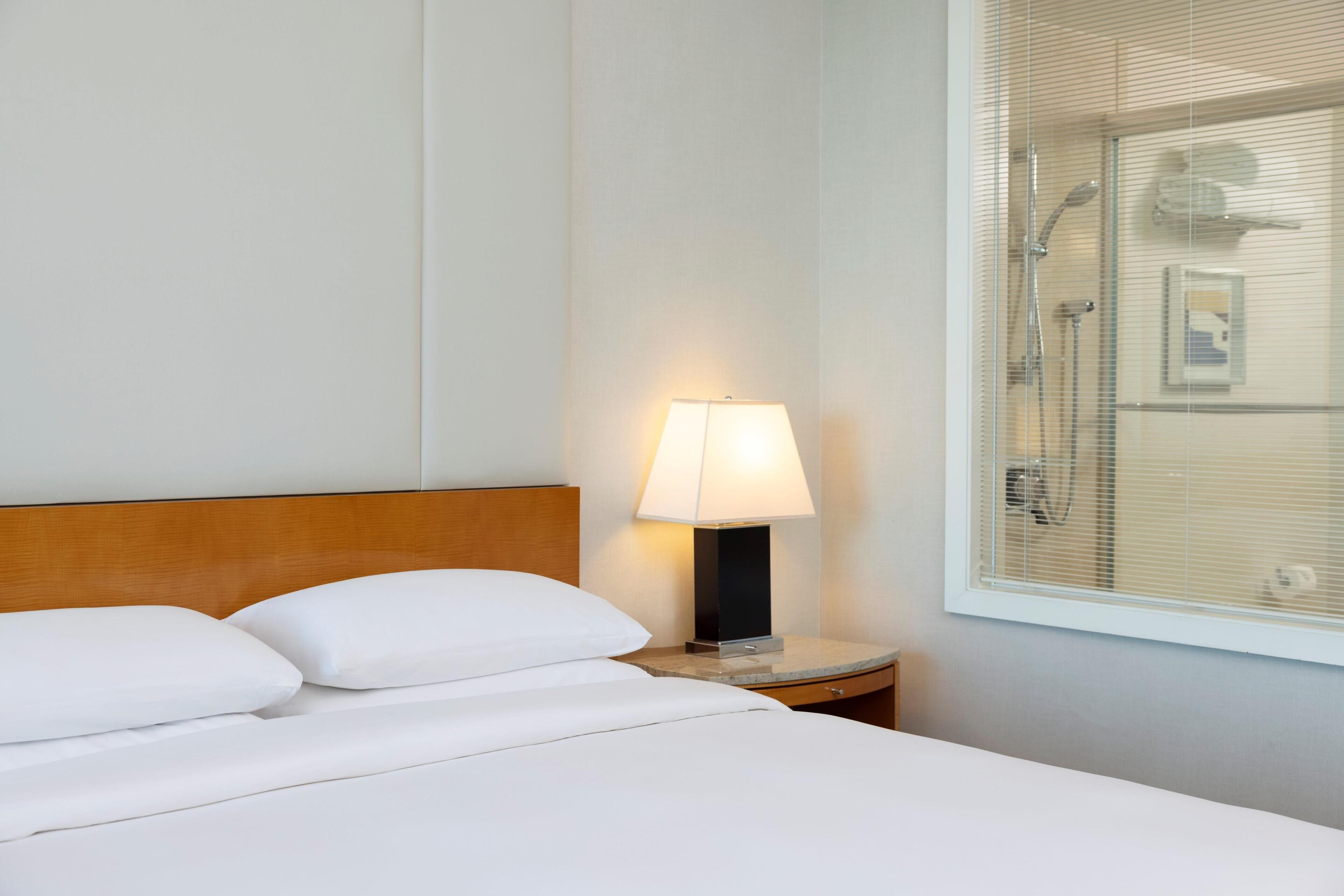 Une chambre d’hôtel avec un lit, une table de chevet avec une lampe et une fenêtre avec des stores.
