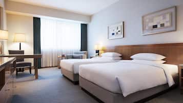 Habitación de hotel con dos camas, un escritorio, una silla, un aparador y un ventanal con cortinas.