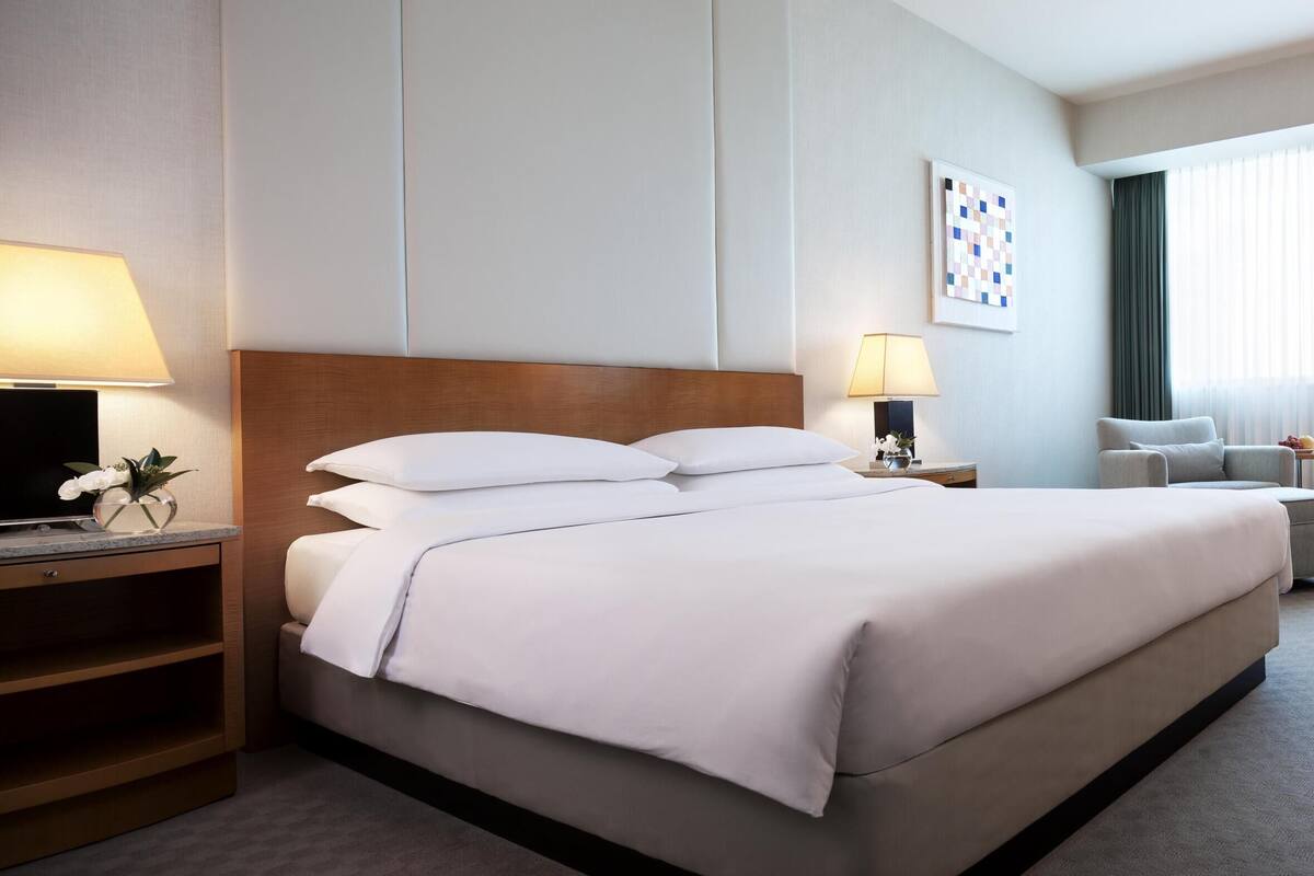 Une chambre d’hôtel avec un lit, un bureau, une chaise, une commode et une lampe.