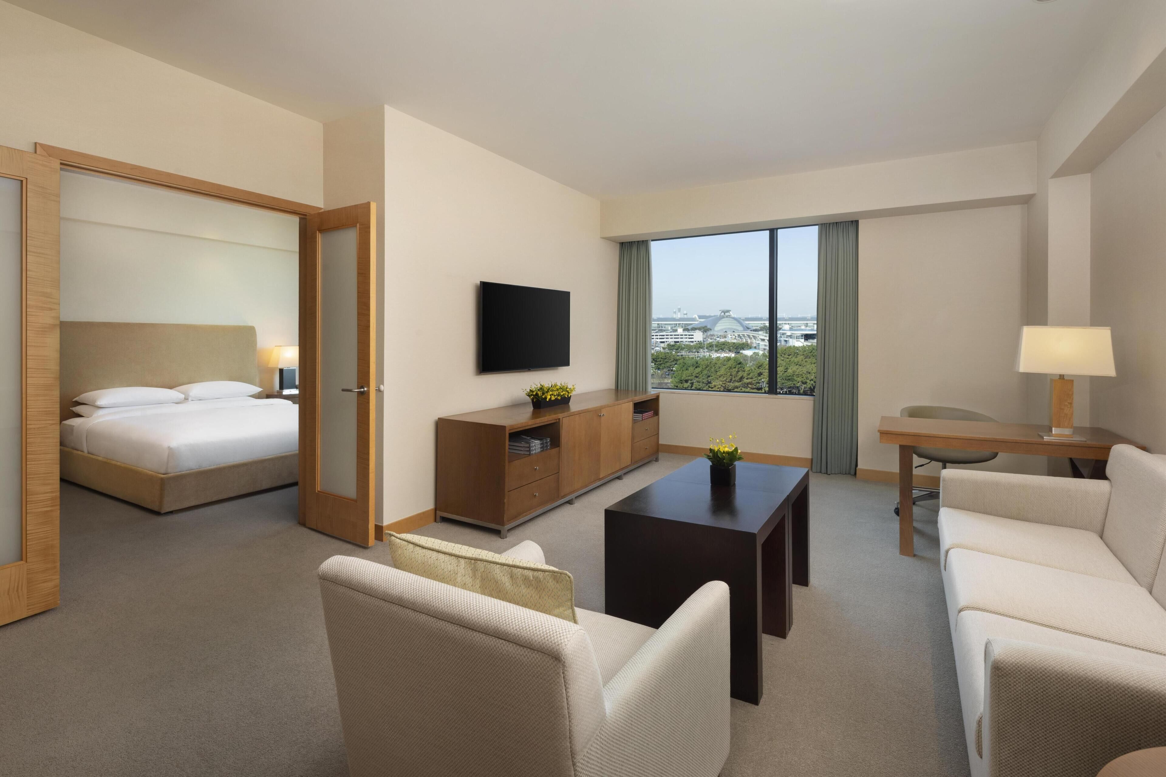 A hotel room with a bed, a TV, a desk, a sofa, and a view of the city.