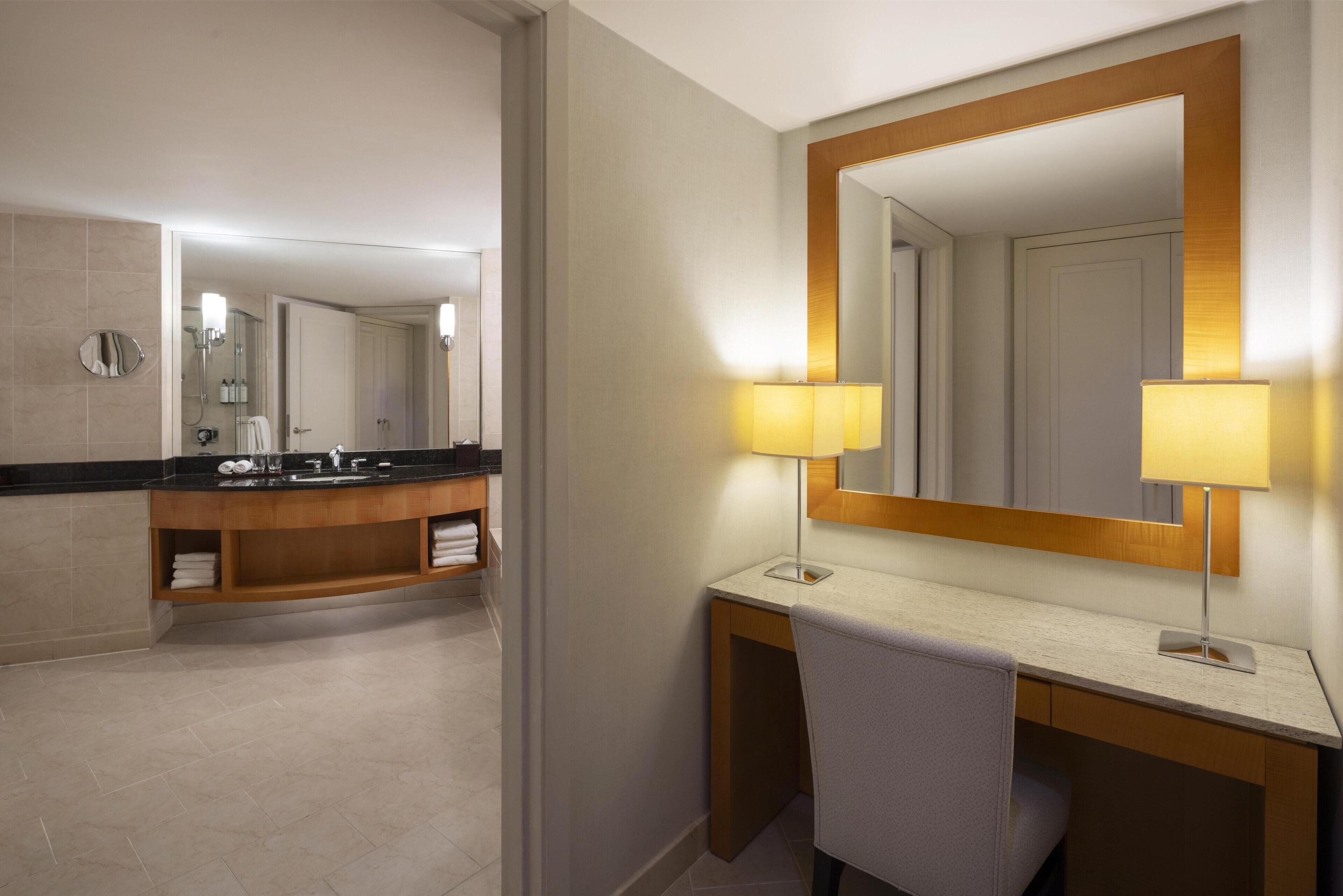 Une salle de bain moderne avec un grand miroir, deux lampes fixées au mur, un meuble-lavabo et une chaise.