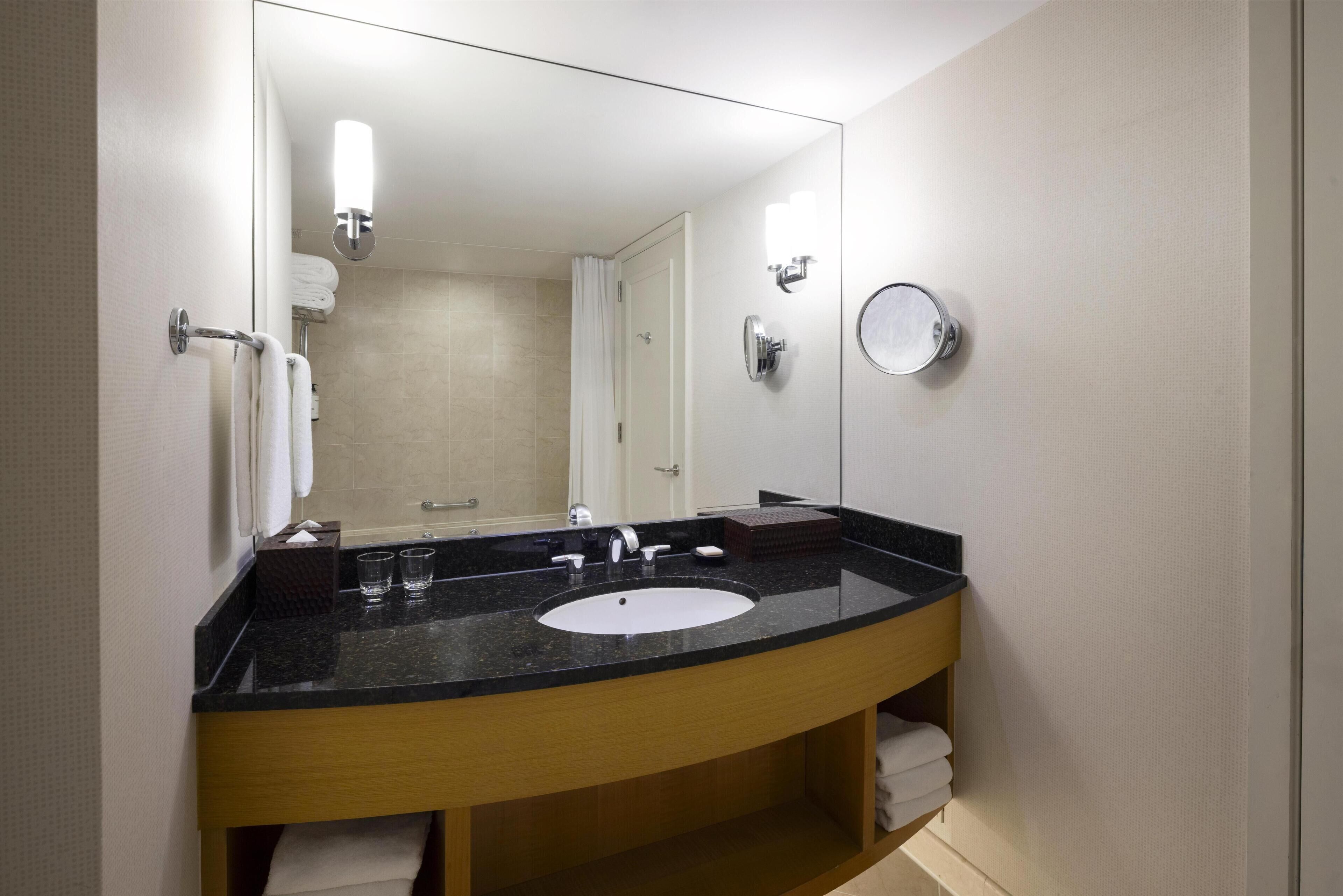A bathroom with a black countertop sink, a mirror, a towel rack, and a round mirror on the wall.