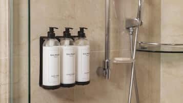 A bathroom with a glass shower enclosure, a handheld showerhead, and three Balmain Paris toiletry bottles mounted on the wall.
