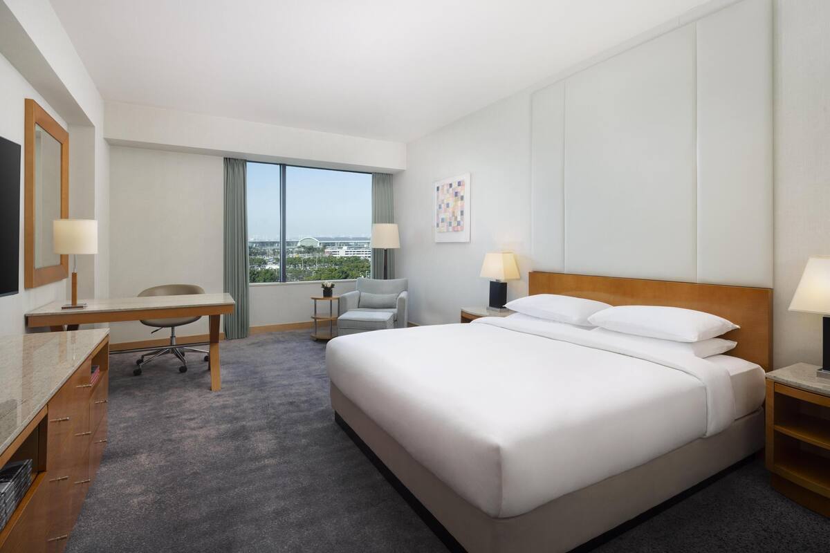Une chambre d’hôtel avec un lit, un bureau, une chaise et une grande fenêtre.