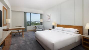 A hotel room with a bed, desk, chair, and large window.
