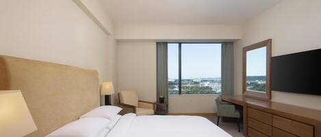 A hotel room with a large bed, a desk, a chair, a TV, and a view of the city.