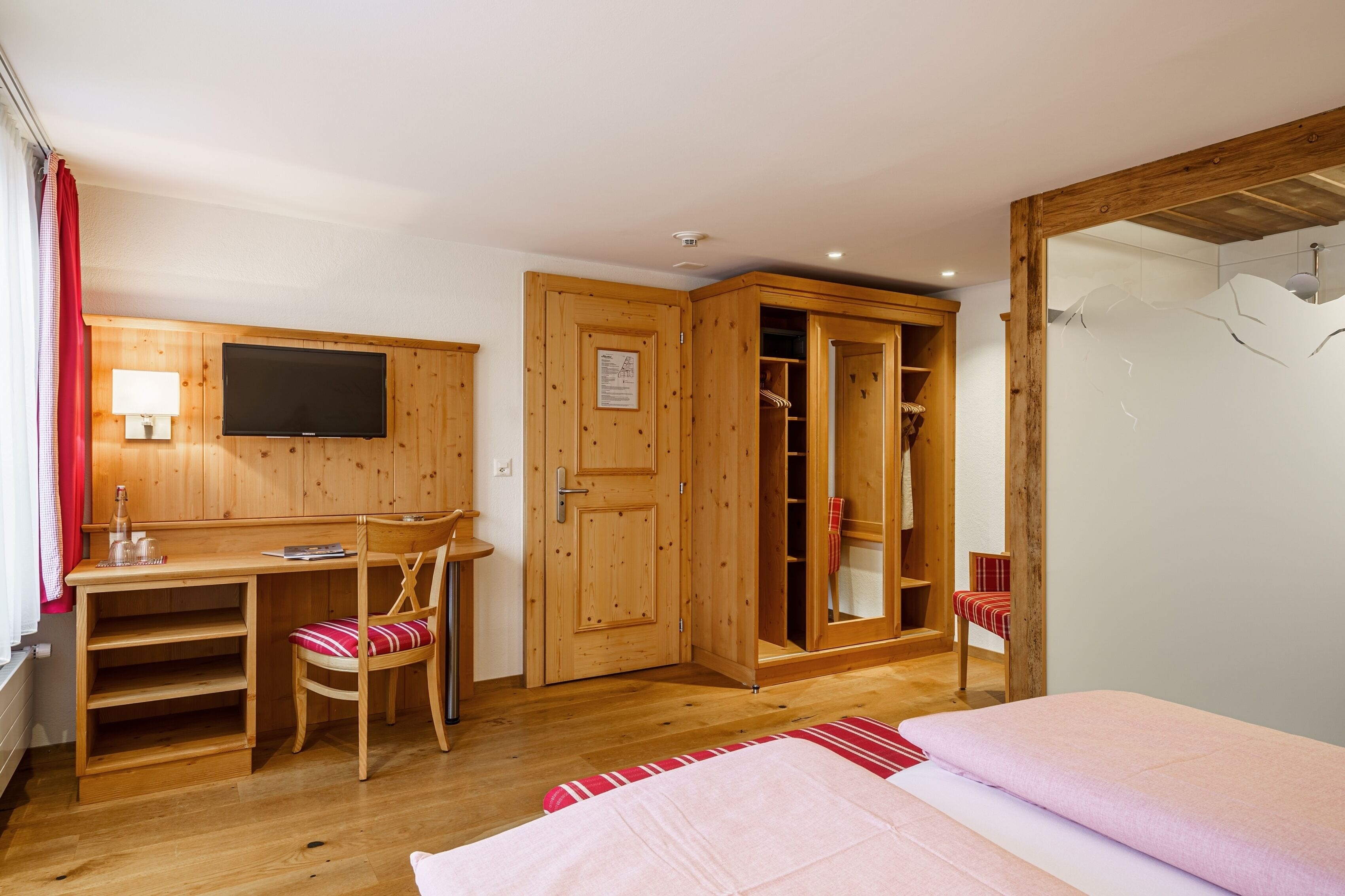 A bedroom with a wooden desk, a TV, a wardrobe, and a bed.