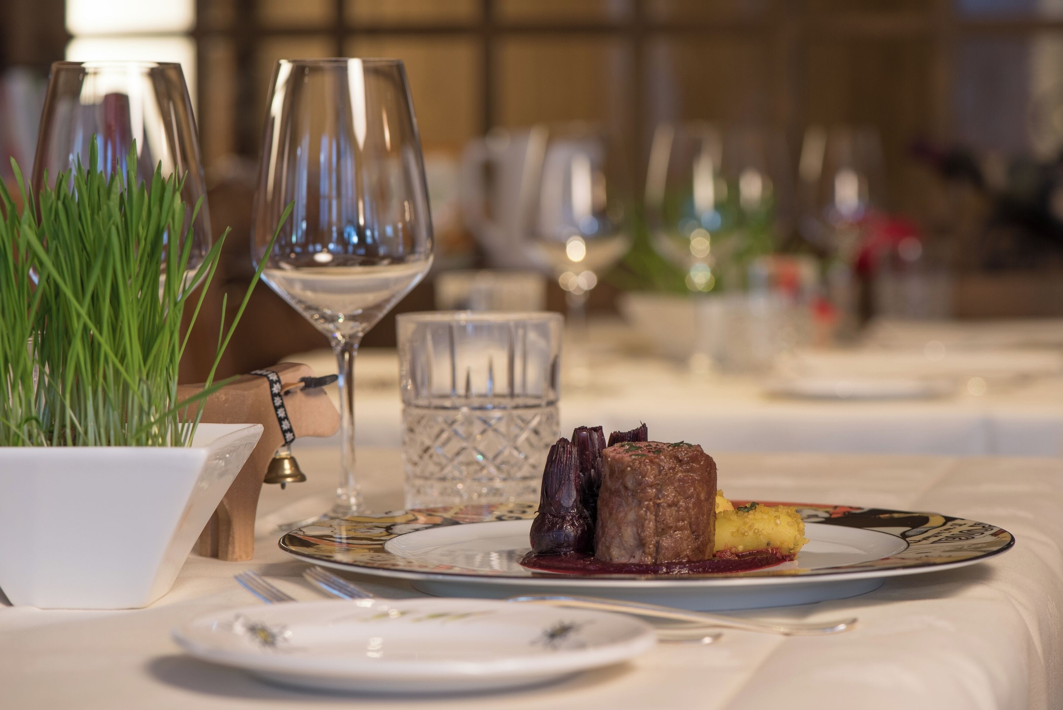 Una mesa de comedor con un plato de comida, un vaso de agua y una planta en maceta.