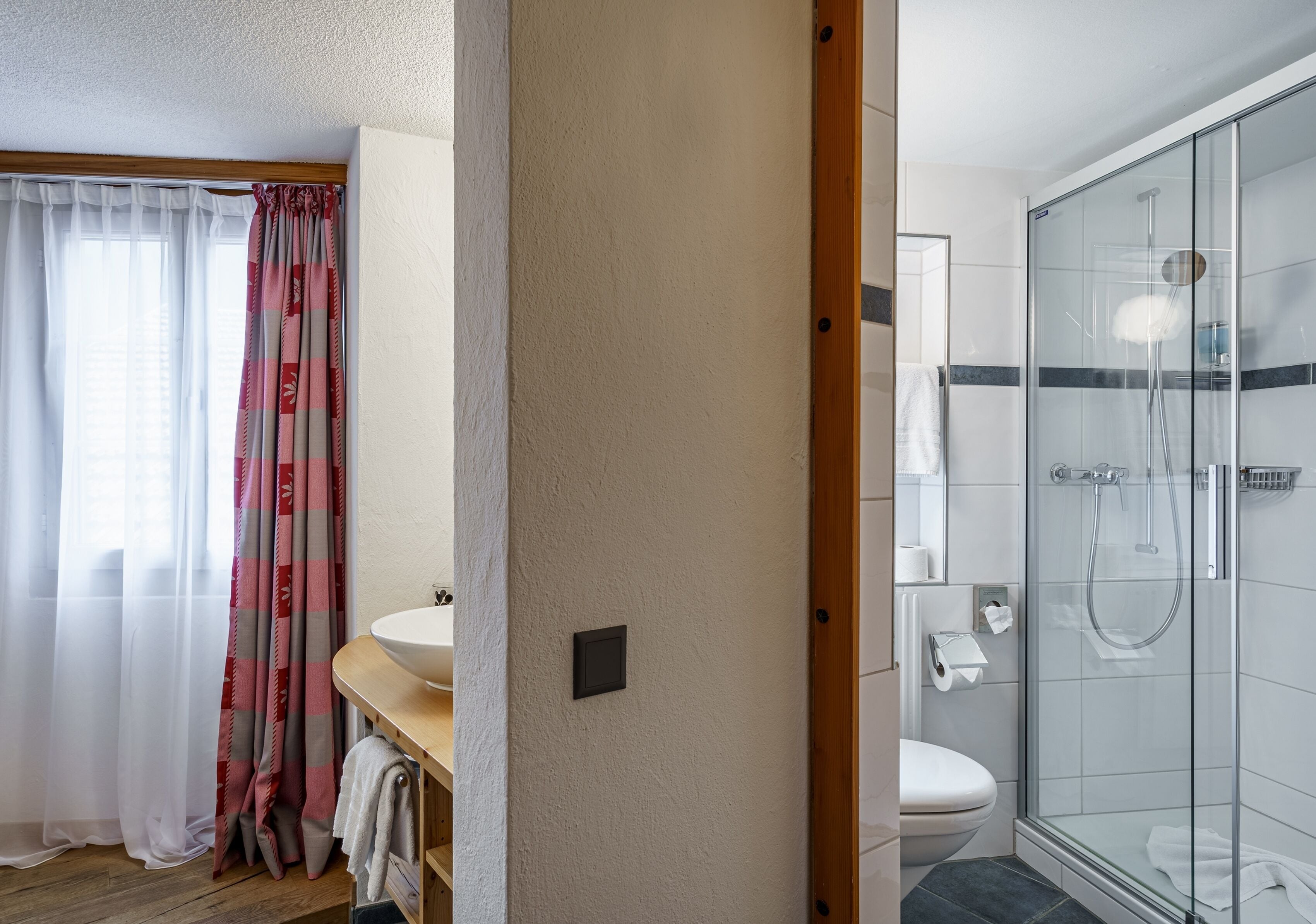Une salle de bain avec une douche à parois de verre, un lavabo blanc et un meuble-lavabo en bois.