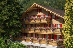 A traditional chalet with multiple balconies adorned with flowers, set against a forested backdrop. - Hotel Alpenblick (Wilderswil)