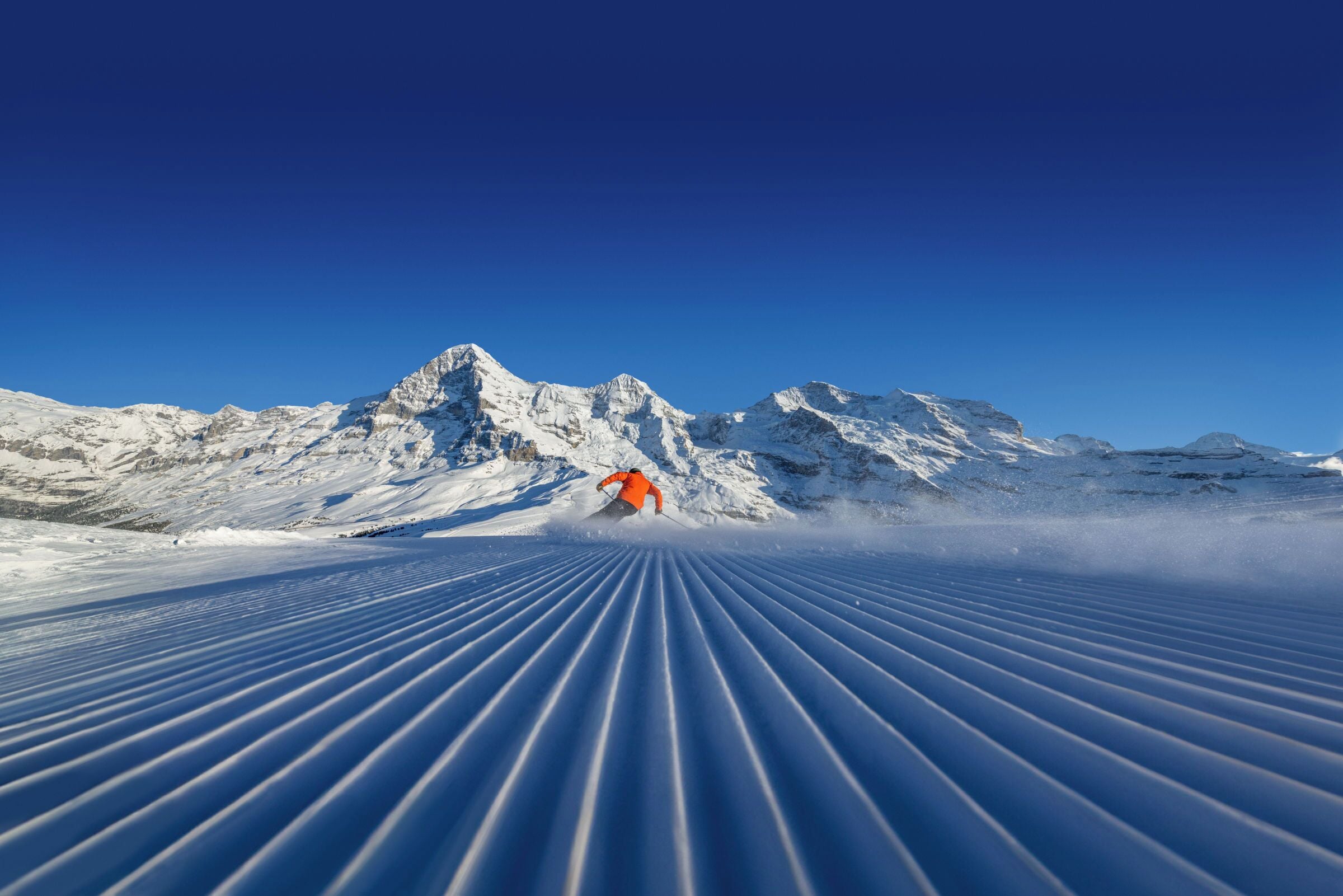 A snowy mountain landscape with a skier in an orange jacket.