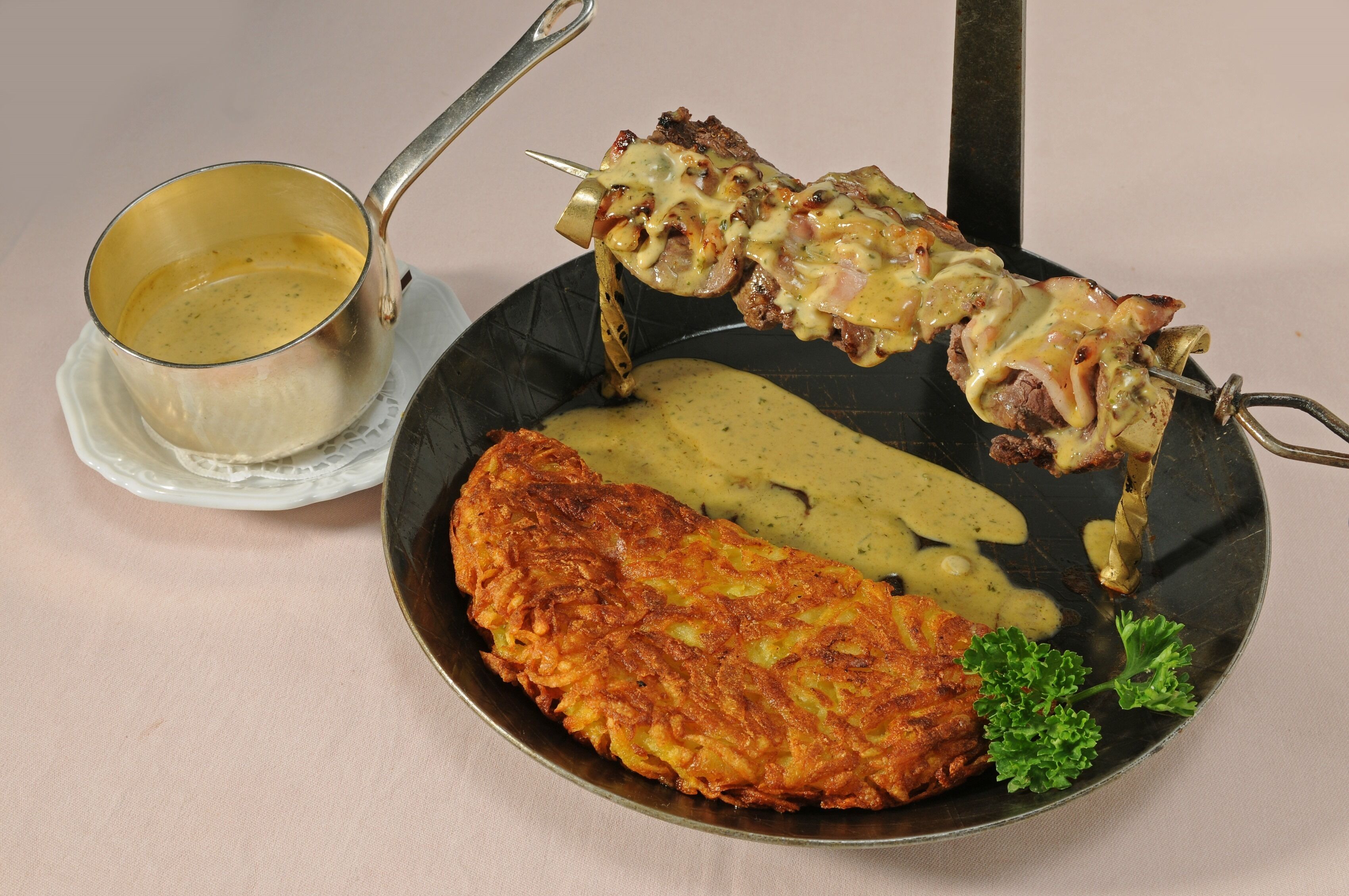 En tallerken med en stegt schnitzel, en spyd med kød og en cremet sovs.