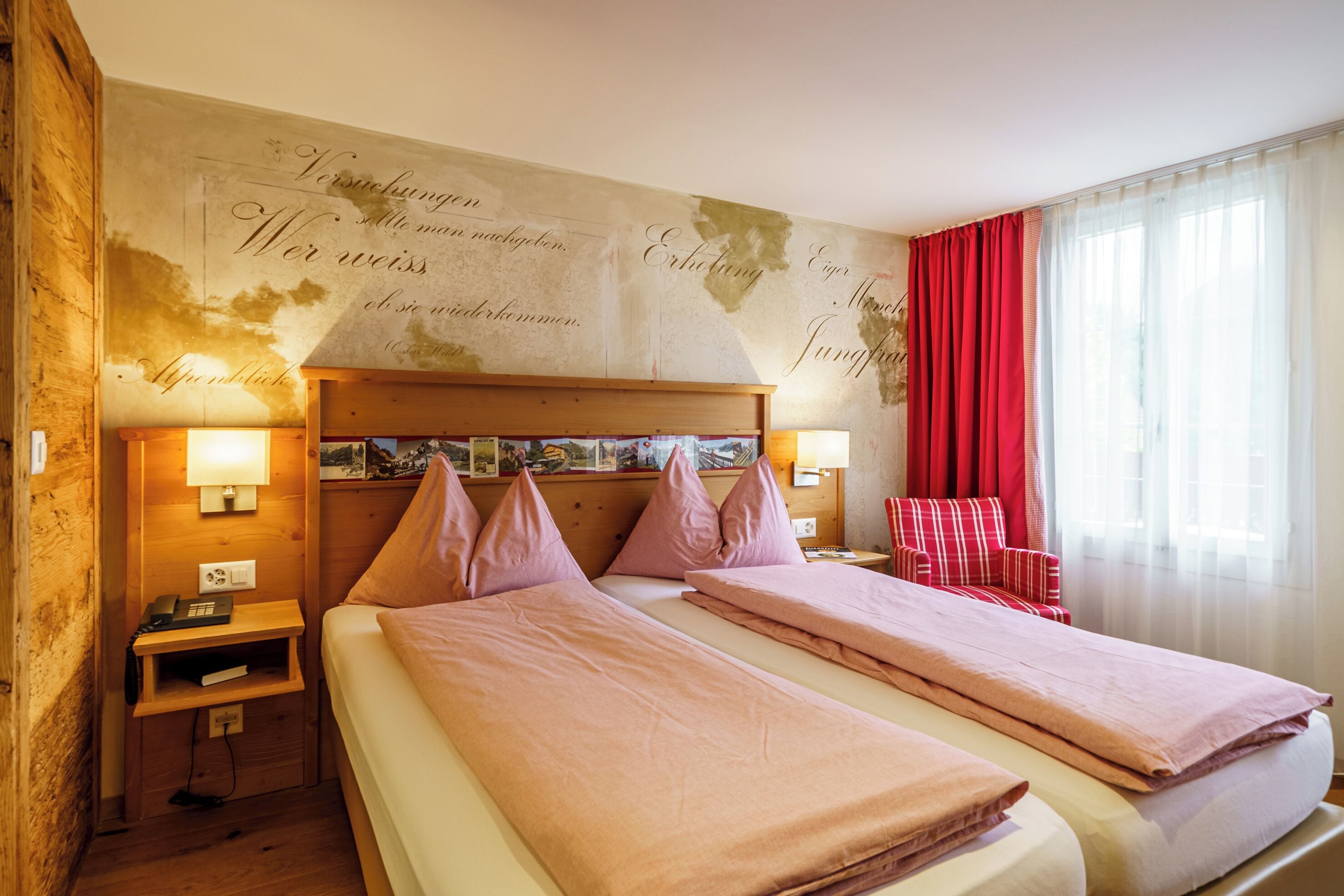 A hotel room with a double bed, two bedside tables, a red chair, and a wall with a map and text.