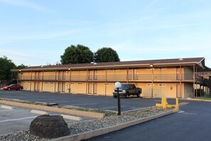 Un motel avec un parking, une voiture rouge et un camion noir garés devant.