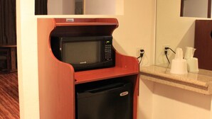 Una kitchenette compacta con microondas y refrigerador, un gabinete de madera y un espejo sobre la encimera.