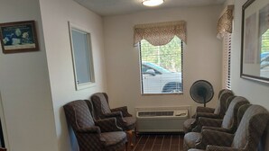 A room with a dark wood floor, a white radiator, a window with blinds, and a wall-mounted fan. - Shelaine Inn (Jeffersonville)