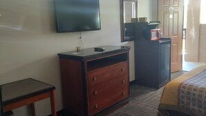 A hotel room with a bed, a desk, a dresser, a television, and a door. - Shelaine Inn (Jeffersonville)