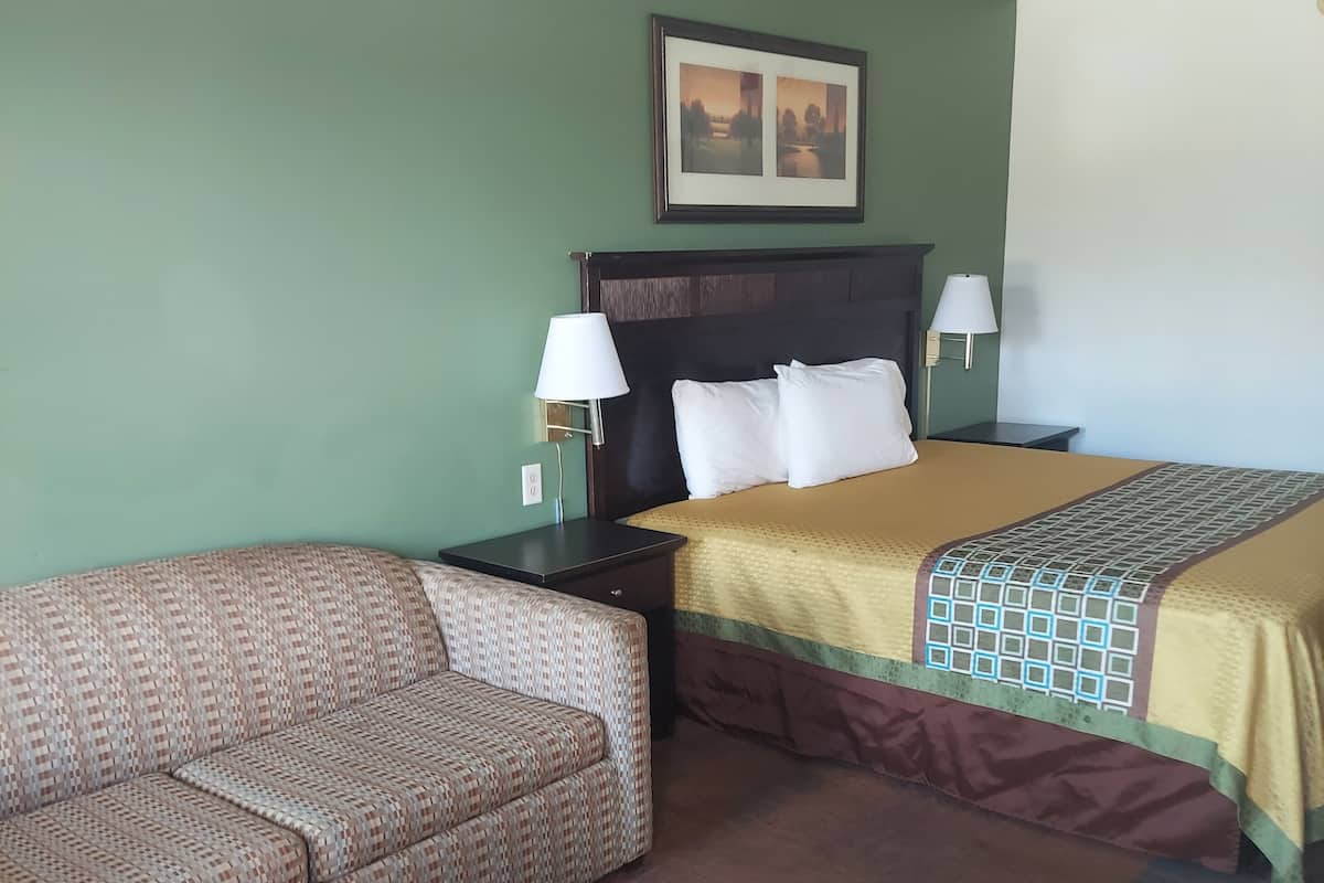 A hotel room with a bed, a sofa, a nightstand, and a wall-mounted lamp.