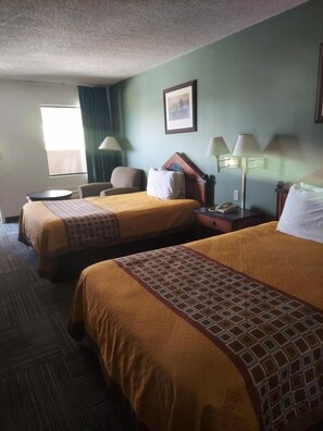 A hotel room with two beds, a desk, a chair, and a window.