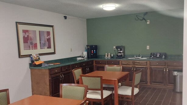 A dining area with wooden tables and chairs, a coffee machine, and a trash bin. - Shelaine Inn (Jeffersonville)