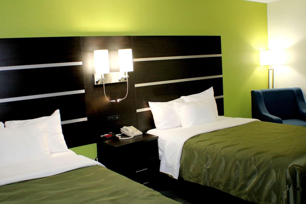 A hotel room with two beds, a nightstand with a phone, and a lamp.