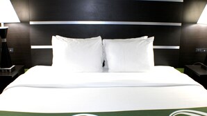 Hotellihuone, jossa on suuri sänky, kaksi valkoista tyynyä, vihreä-valkoinen kuviollinen päiväpeite ja tumma pääty, jossa on vaakasuorat linjat.