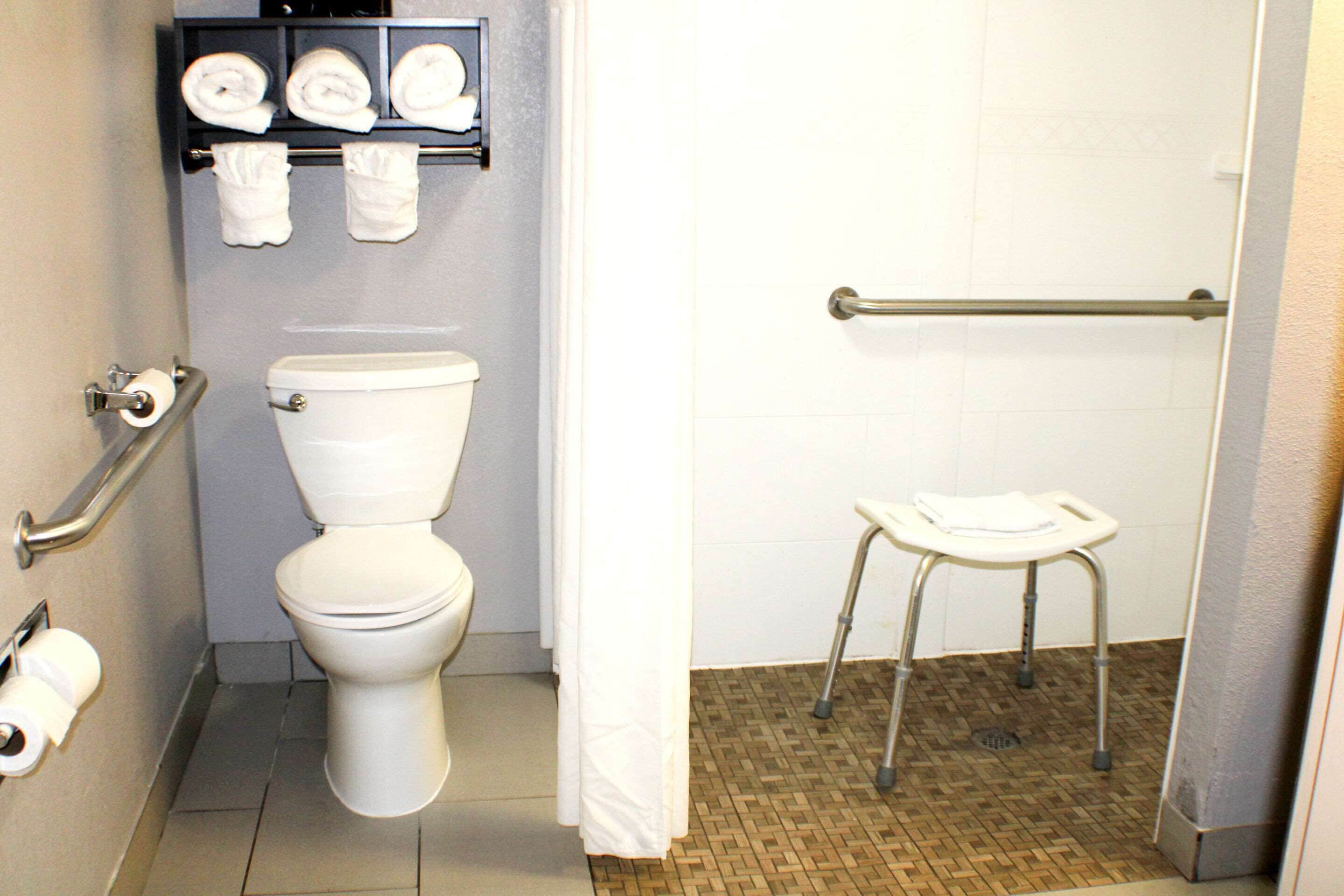 A bathroom with a toilet, a handrail, a shelf with towels, and a wheelchair-accessible bench.