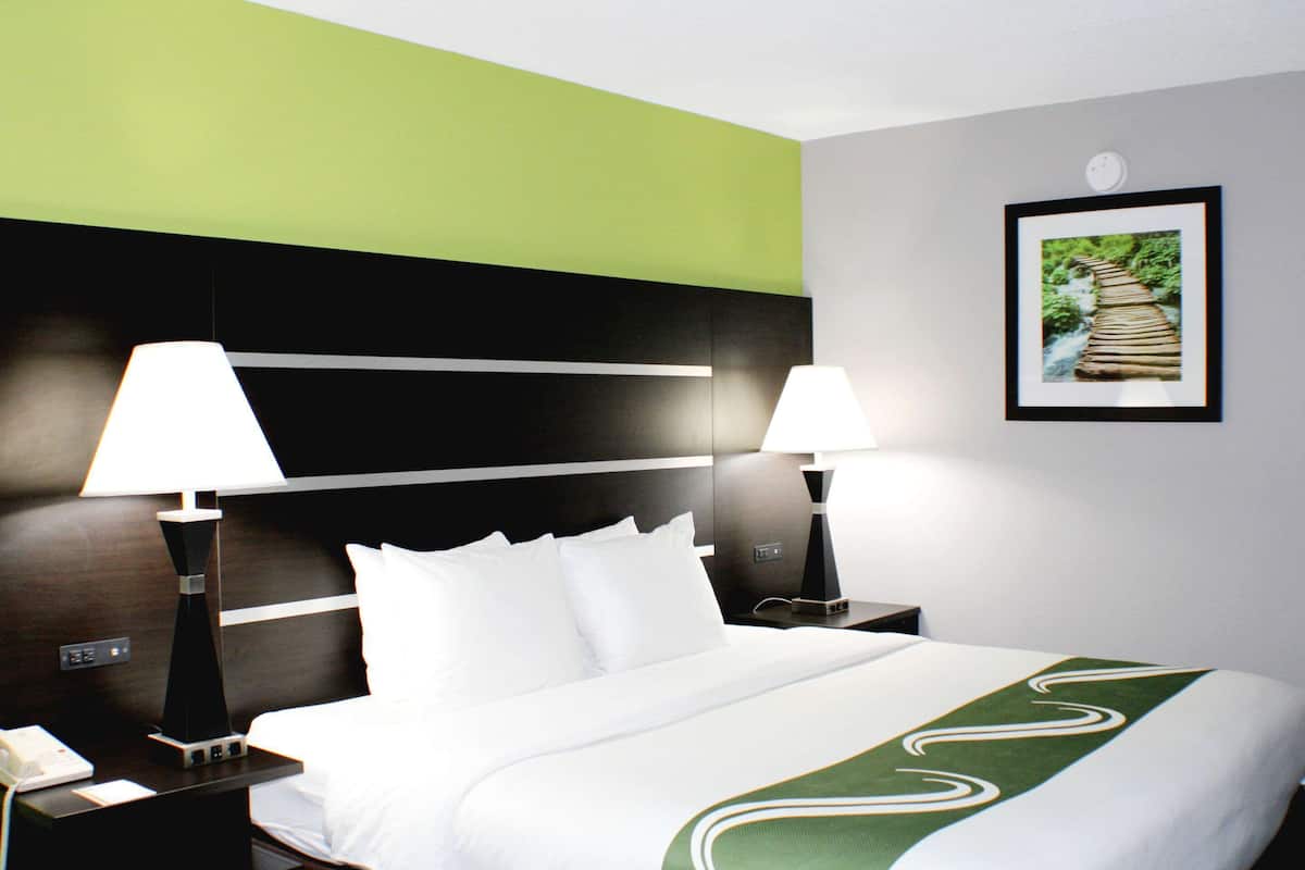 A hotel room with a bed, two bedside lamps, a nightstand with a phone, and a framed picture on the wall.