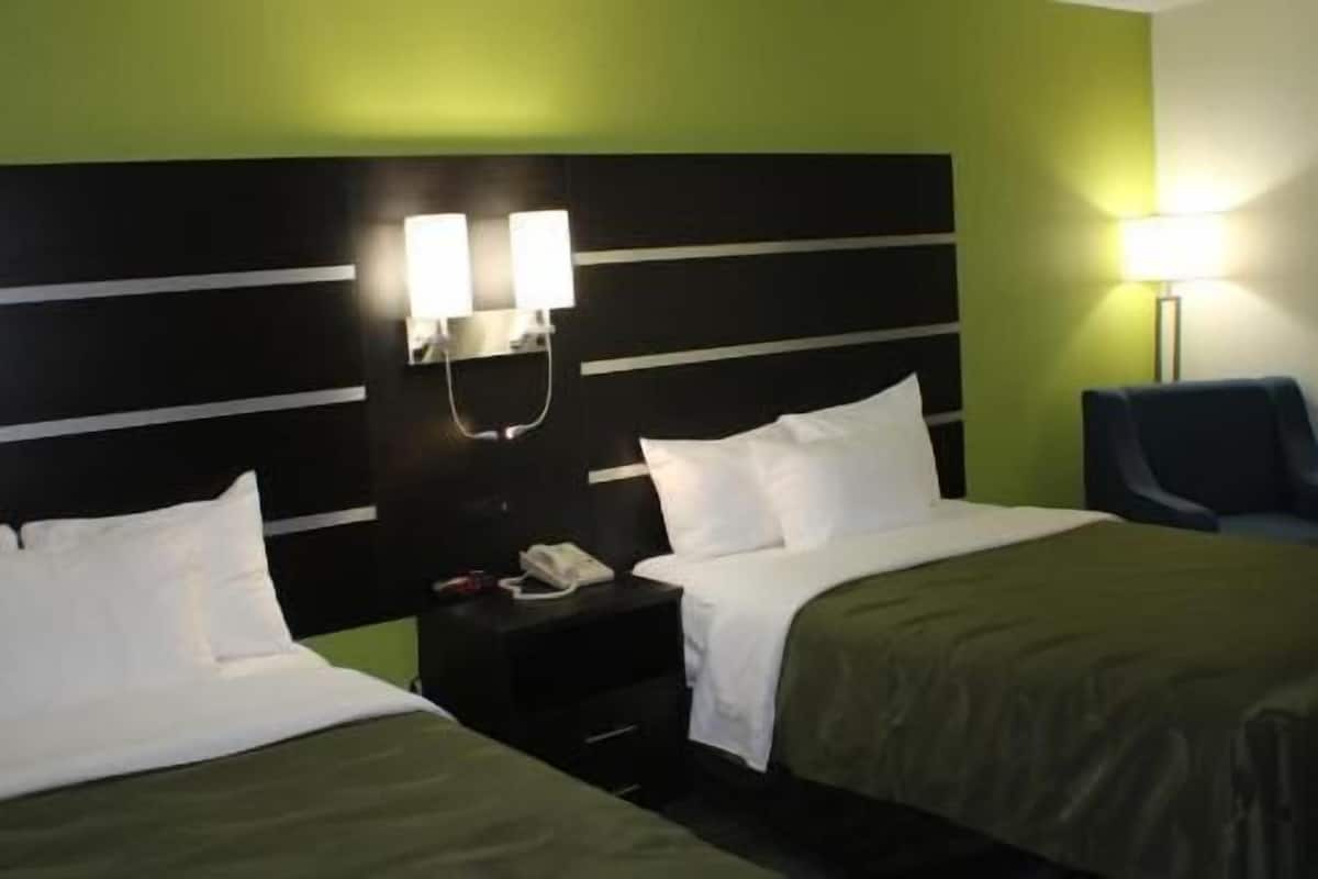A hotel room with two beds, a nightstand with a phone, and a lamp.