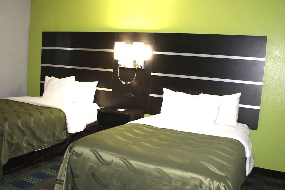 A hotel room with two beds, a nightstand, and a wall-mounted light fixture.
