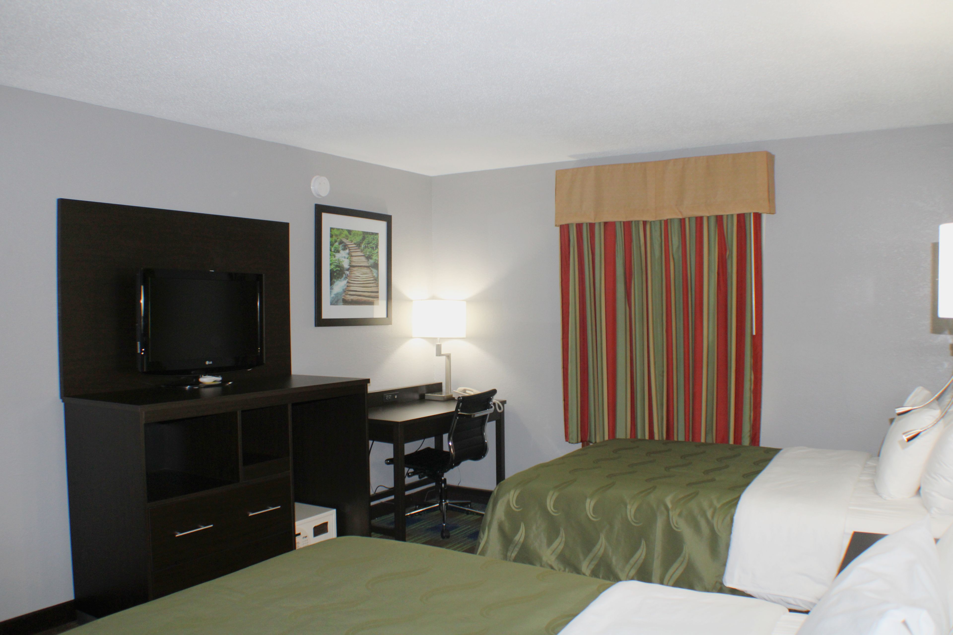 A hotel room with two beds, a desk with a chair, a television, and a lamp.