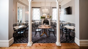 A dining area with a black and white patterned floor, white columns, and a chandelier. Tables and chairs are arranged for dining. - Salamanca Terraces (Battery Point)