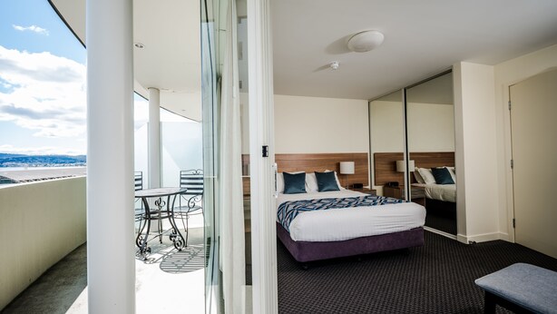 A hotel room with a bed, bedside tables, a chair, a balcony with a table and chairs, and a view of the sea. - Salamanca Terraces (Battery Point)