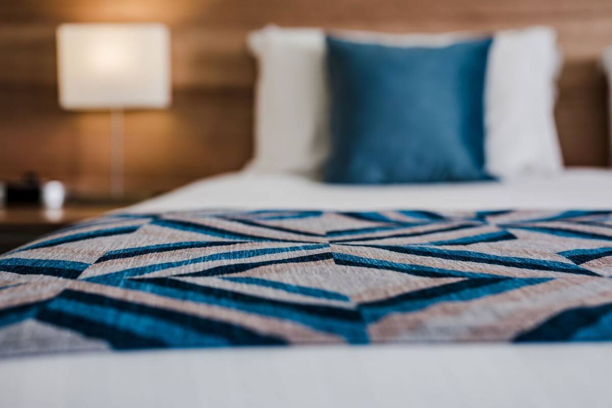 A bed with a geometric patterned blanket, a blue pillow, and a wooden headboard.
