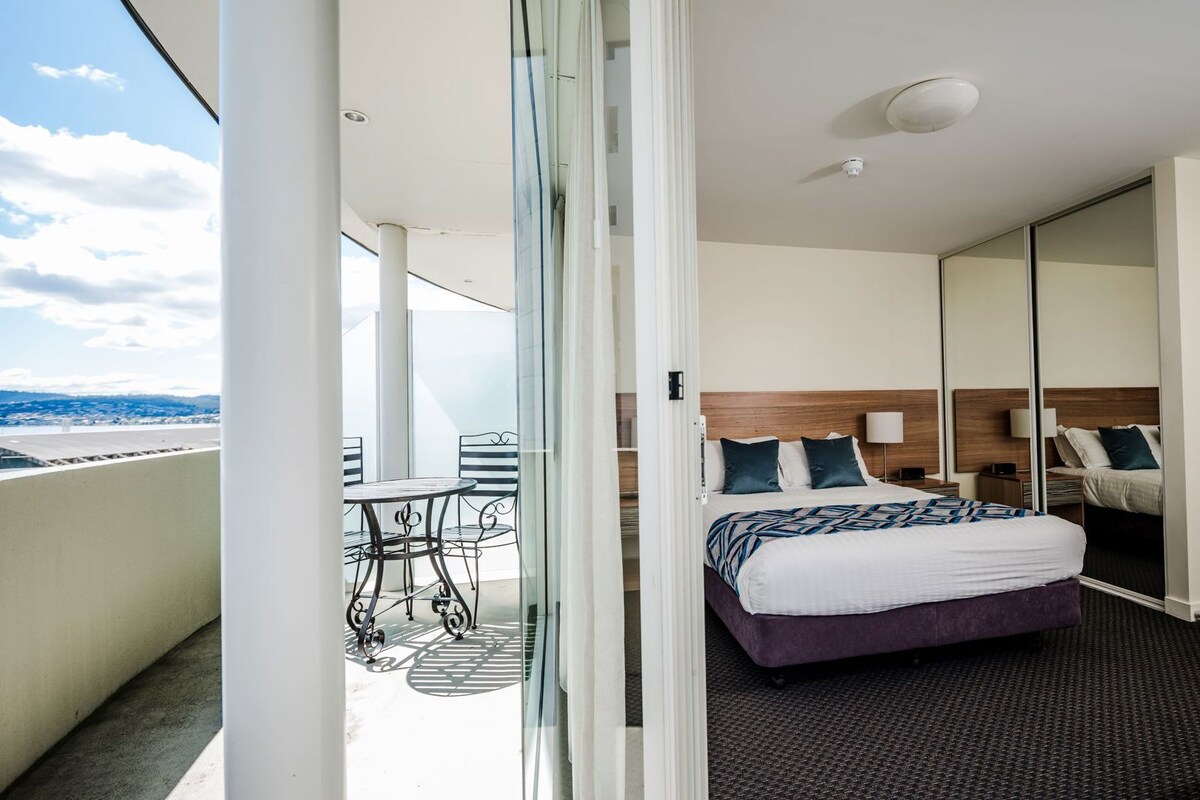 Ein Hotelzimmer mit Bett, Schreibtisch, Stuhl, einem kleinen Tisch und einem Balkon mit Aussicht.