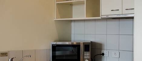 Een moderne keuken met een magnetron, oven en vaatwasser. Op een plank boven de magnetron staan een wijnfles en glazen.