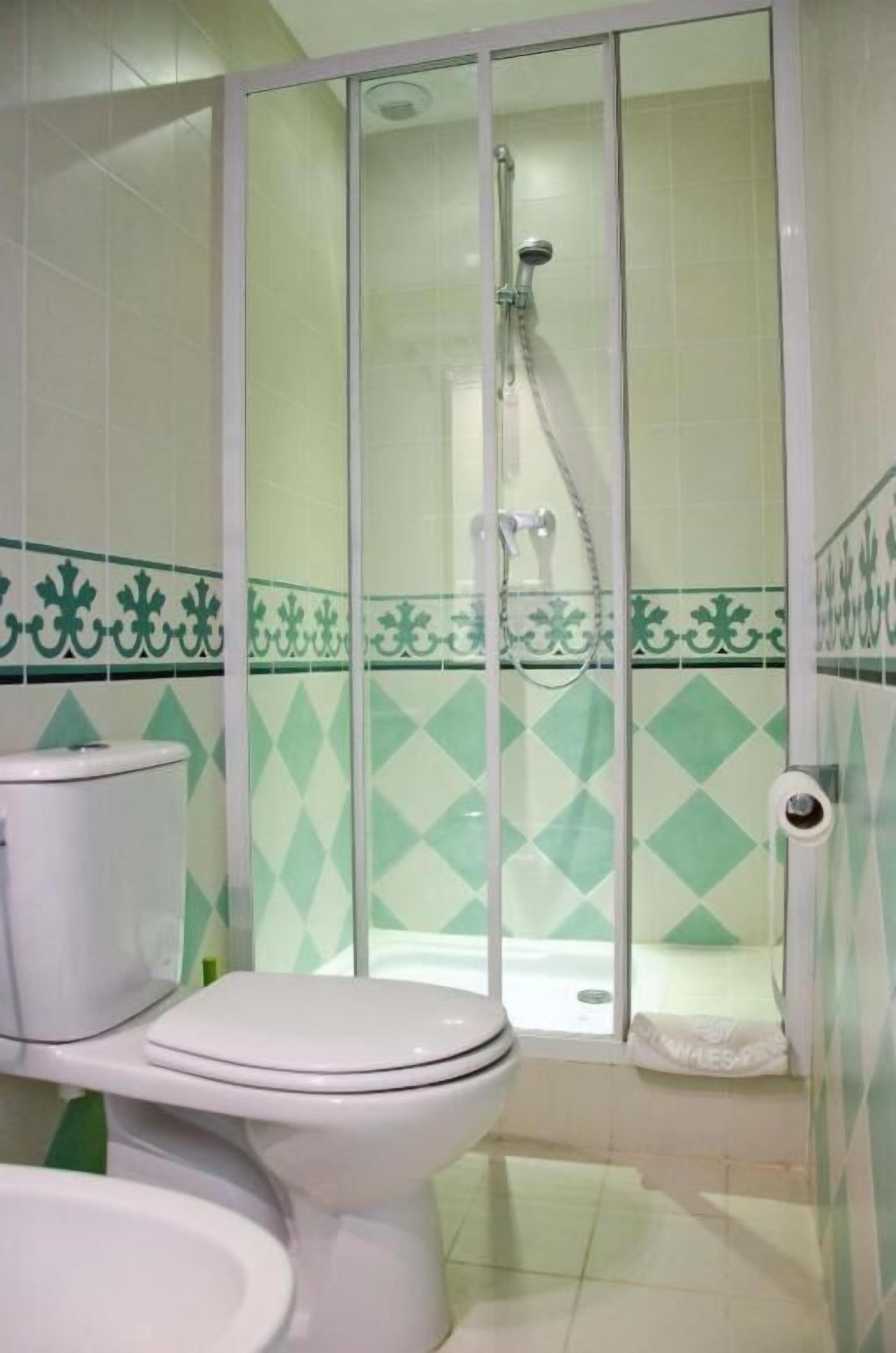 Un baño con inodoro, cabina de ducha y azulejos verdes en patrón de rombos.