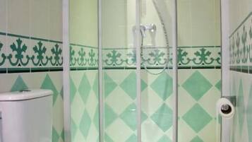 Un baño con inodoro, cabina de ducha y azulejos verdes en patrón de rombos.