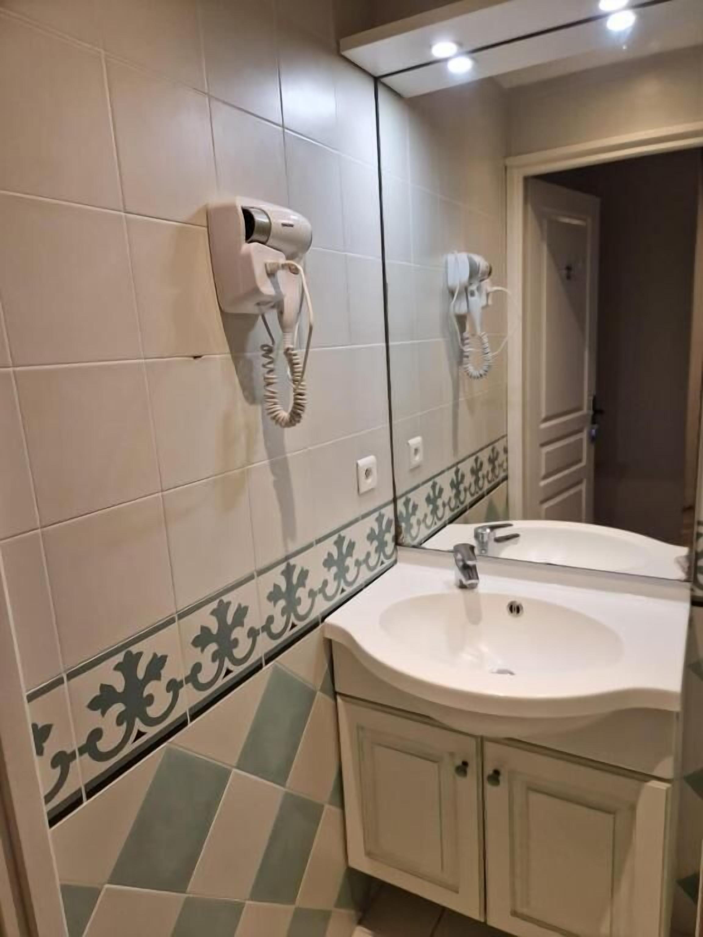 A bathroom with a white sink, a mirror, and two hair dryers mounted on the wall.