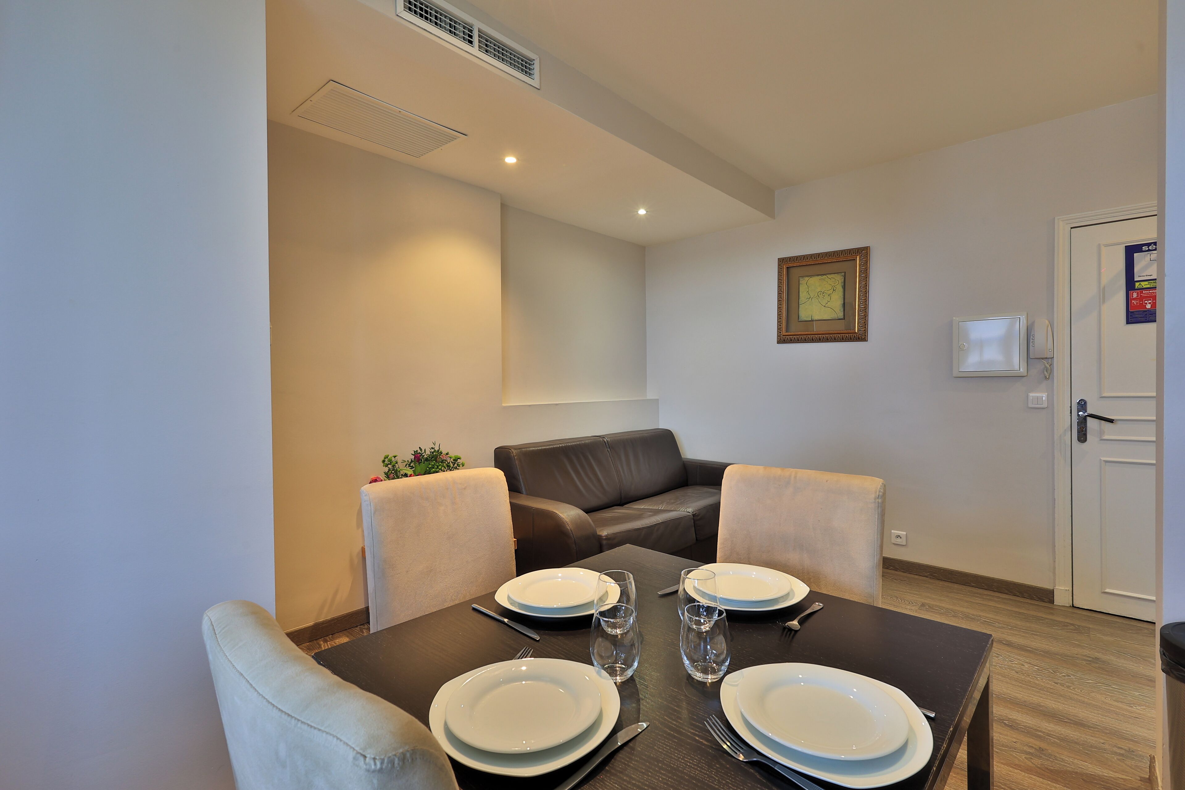 Un coin repas avec une table dressée pour quatre personnes, un canapé et une porte dotée d’une serrure.