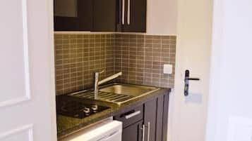 A compact kitchen with dark cabinets, a stainless steel sink, and a white dishwasher.