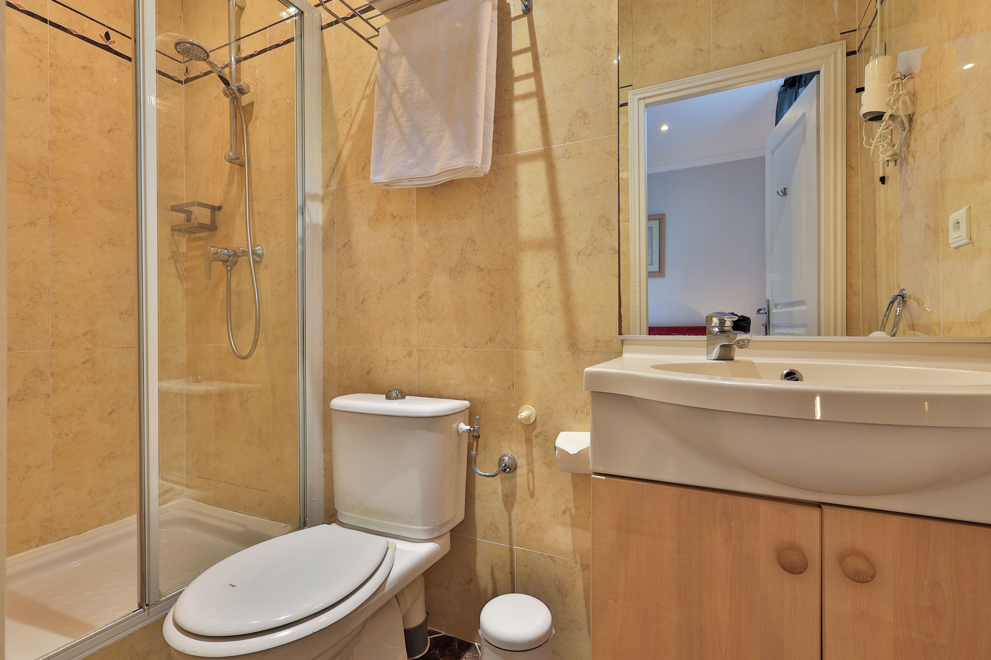 Baño con cabina de ducha de vidrio, inodoro, lavamanos y armarios de madera.