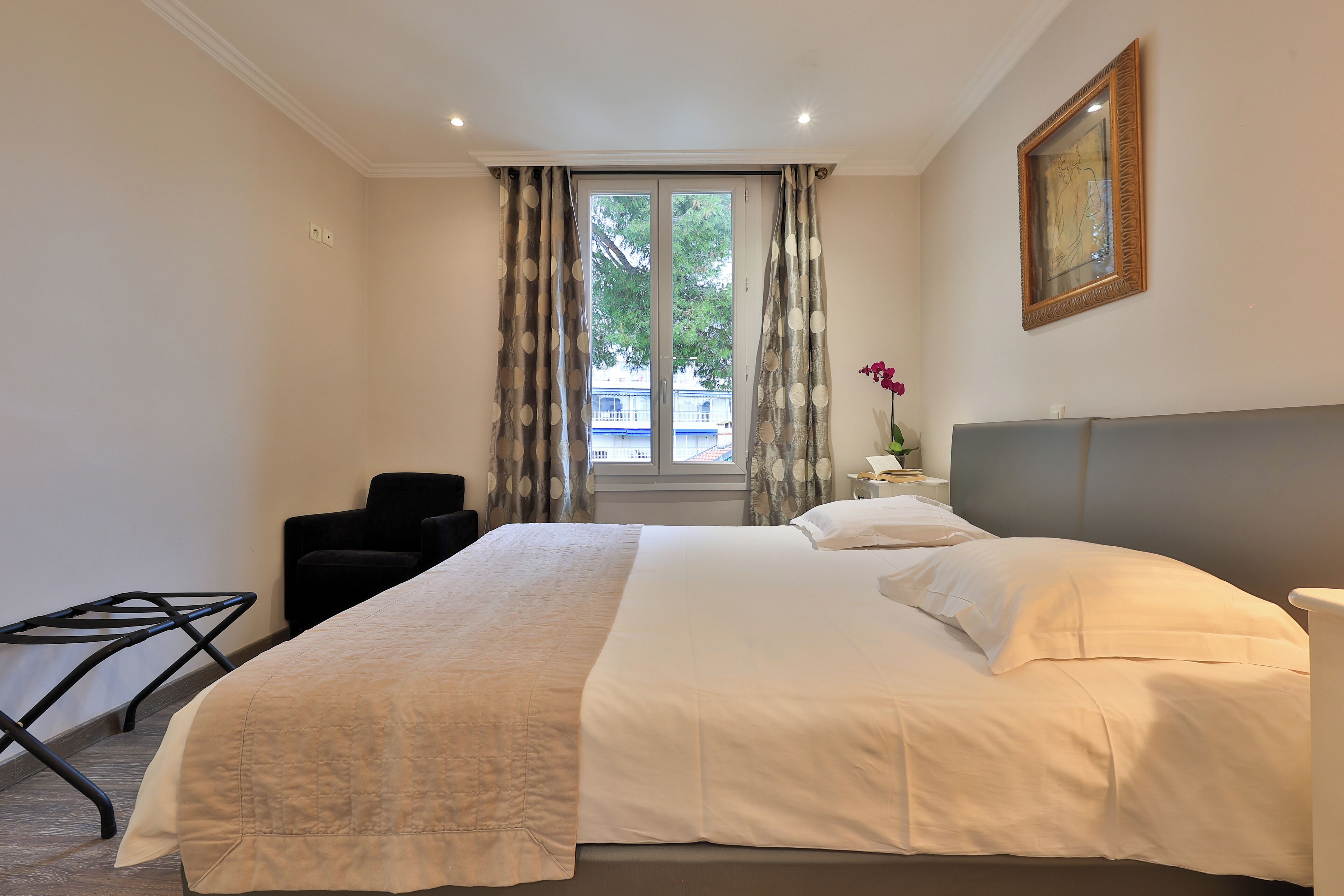 Quarto de hotel com cama grande, uma cadeira, escrivaninha e janela com cortinas.