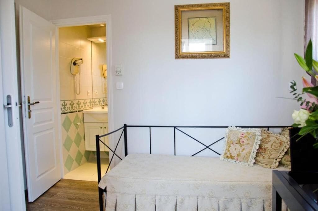 A bedroom with a bed, a bedside table, a framed picture on the wall, and a bathroom visible through an open door.