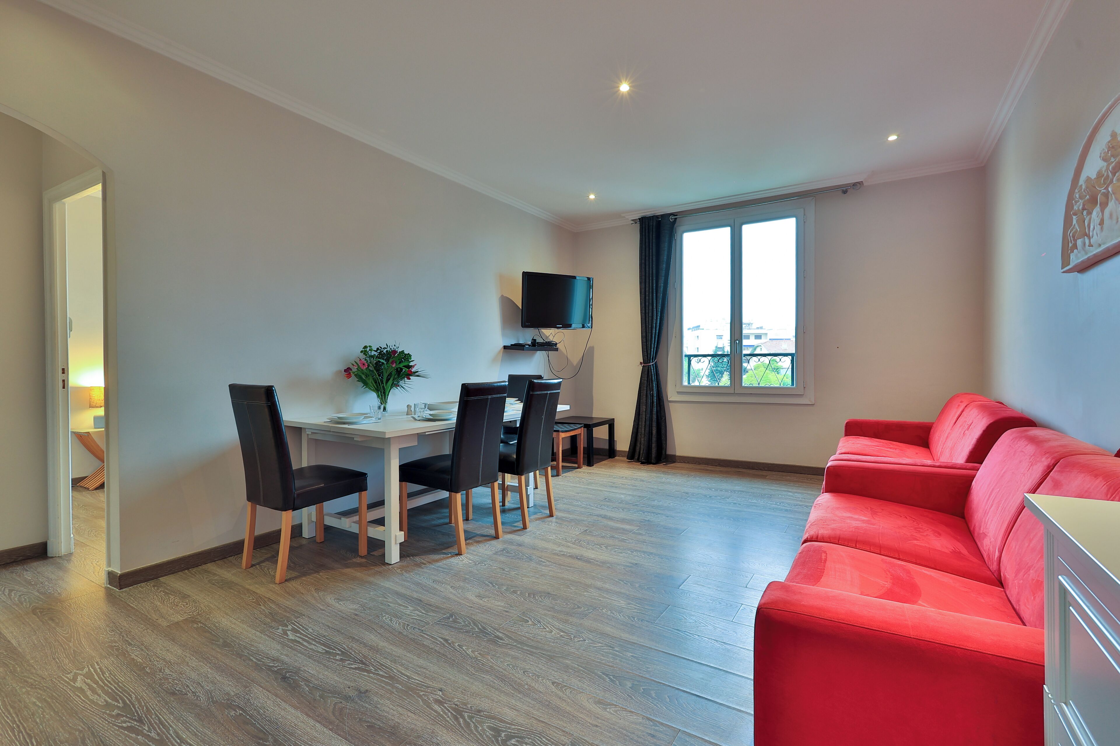 Una sala moderna con un sofá rojo, un comedor con una mesa y sillas, y un televisor montado en la pared.
