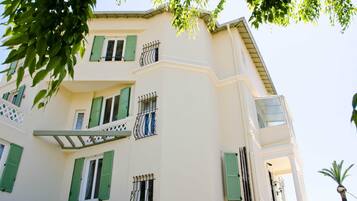 Un immeuble à plusieurs étages, doté de balcons, de volets verts et d’une façade blanche.