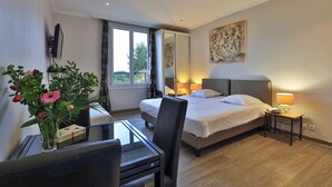 Una habitación de hotel con cama, mesita de noche, silla, escritorio y ventana con cortinas.