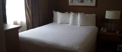 A hotel room with a large bed, a bedside table, a lamp, and a clock.
