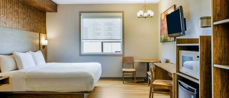A hotel room with a bed, a desk, a chair, a TV, a microwave, and a refrigerator.
