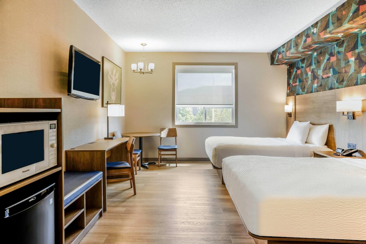 A hotel room with two beds, a desk with a chair, a television, a microwave, and a window with blinds.